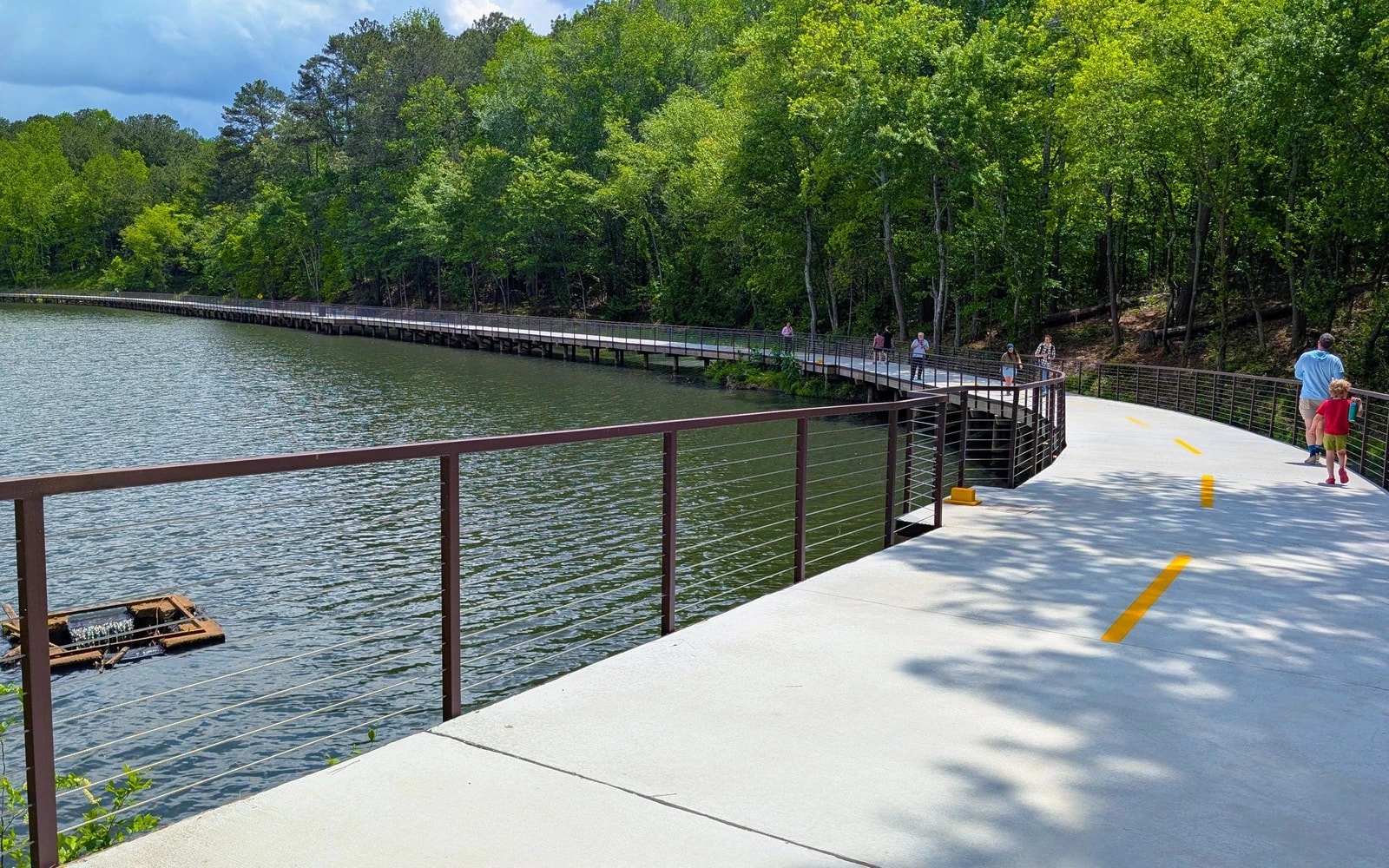 A family and other visitors walk a broad, curving path beside the water at Sandy Springs’ Springway–Morgan Falls Connector.