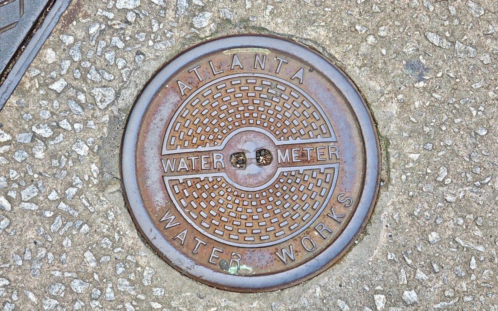Round Atlanta Water Works meter cover set into a rough concrete sidewalk.