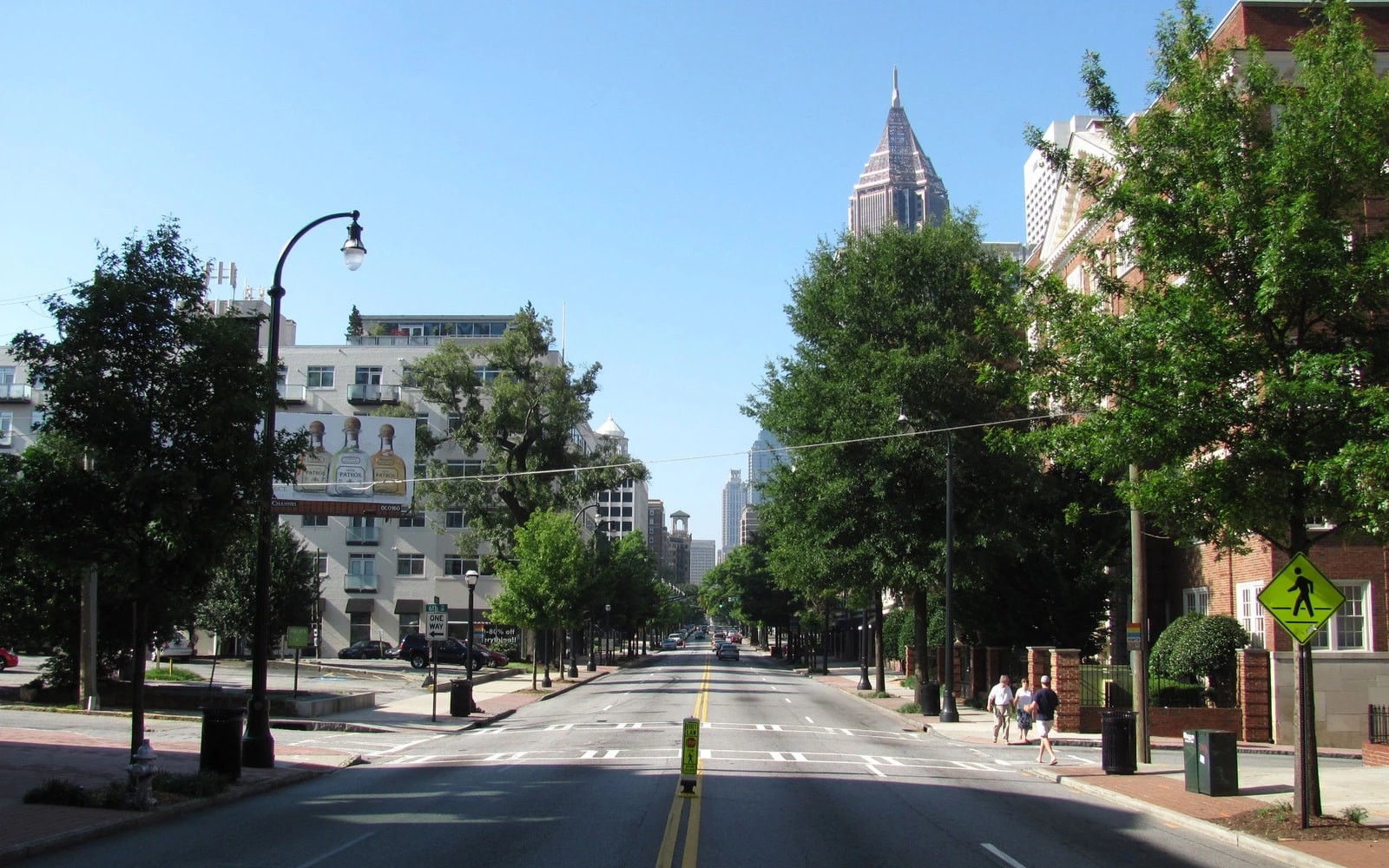 View down Peachtree Street at Sixth Street in Midtown Atlanta, showing vehicle lanes, sidewalks, a marked crosswalk, a pedestrian crossing sign and two people on the sidewalk.