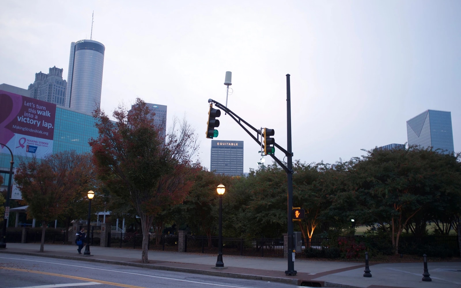 Traffic signals and a pedestrian signal at a downtown Atlanta intersection, with high-rise buildings behind trees.