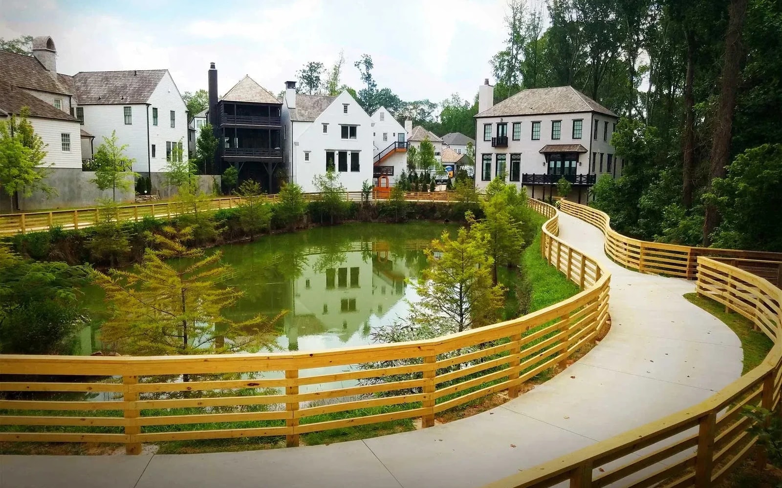 A pond edged by homes and trees, with a curved wooden-railed boardwalk alongside it.