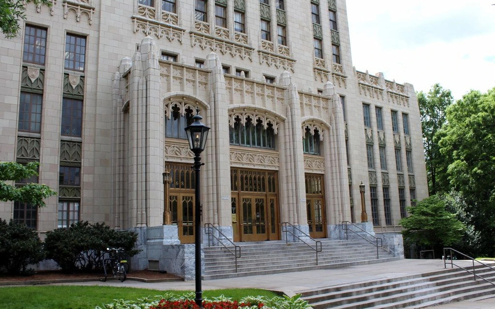 Front entrance and ornate stone facade of Atlanta City Hall, with steps, a lamp post and landscaping in the foreground.