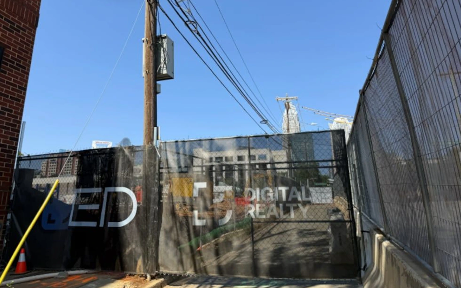Digital Realty construction site behind chain-link fencing, with utility lines overhead, in Uptown Charlotte.