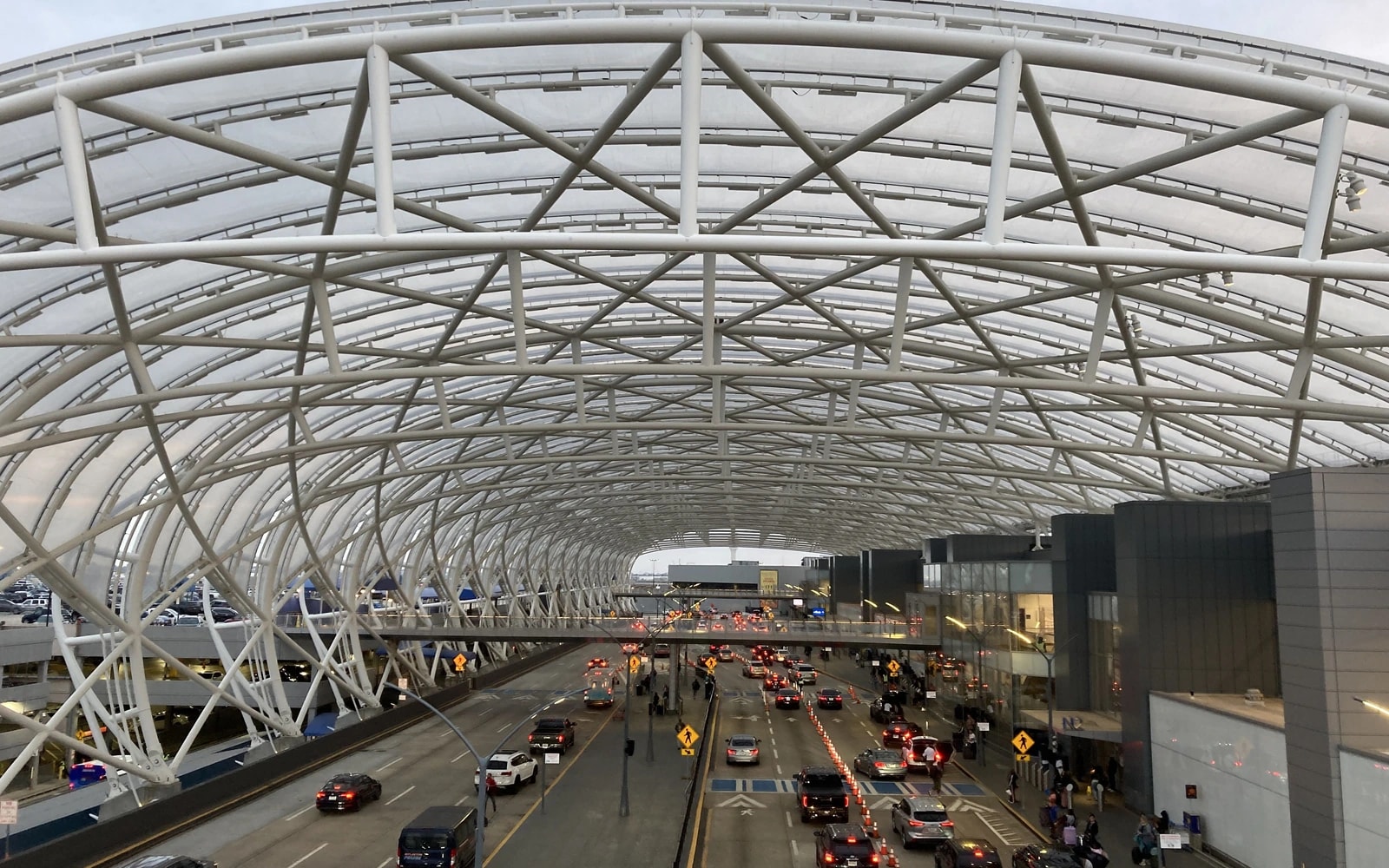Cars occupy multiple terminal access lanes beneath a sweeping white steel canopy at Hartsfield-Jackson Atlanta International Airport.